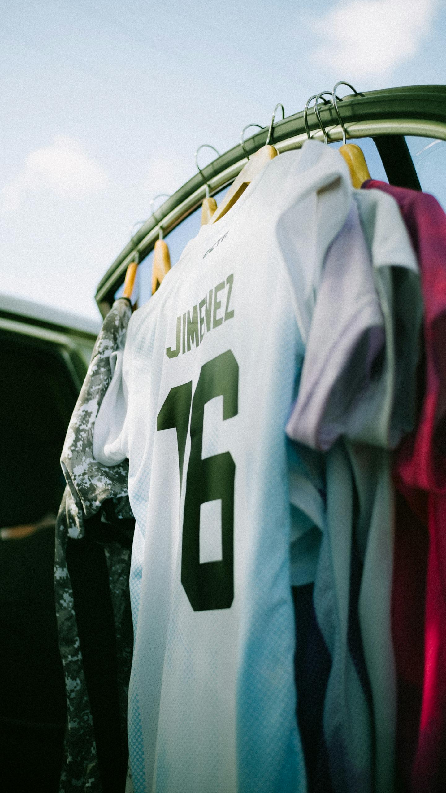A Jersey Dress white soccer jersey with the number 16 hangs among colorful clothes on a rack.