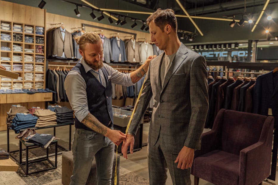 Clothing Brands Men’s Clothing Tailor measuring a customer in a suit store for a perfect fit.