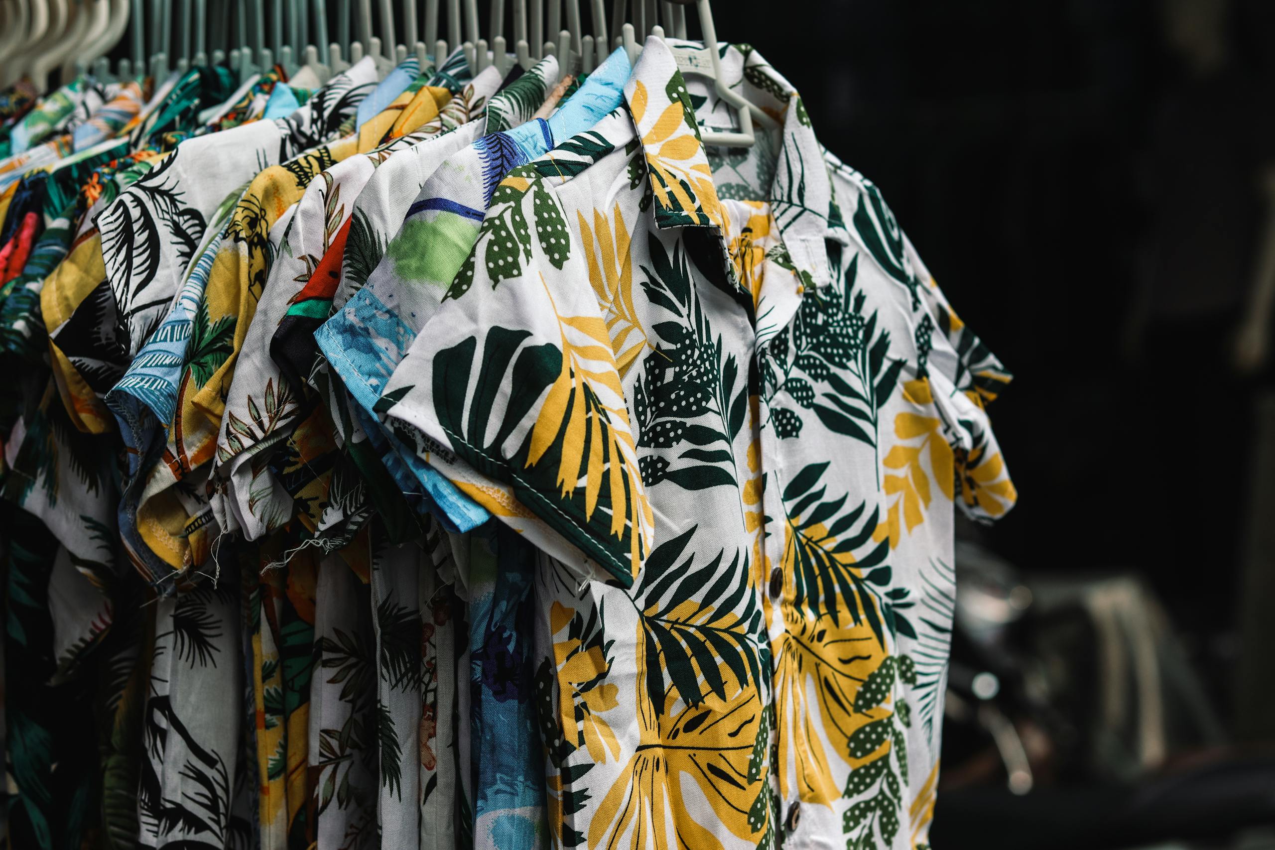 A collection of Button-Down Shirts vibrant tropical print shirts hanging on a rack in a retail store.