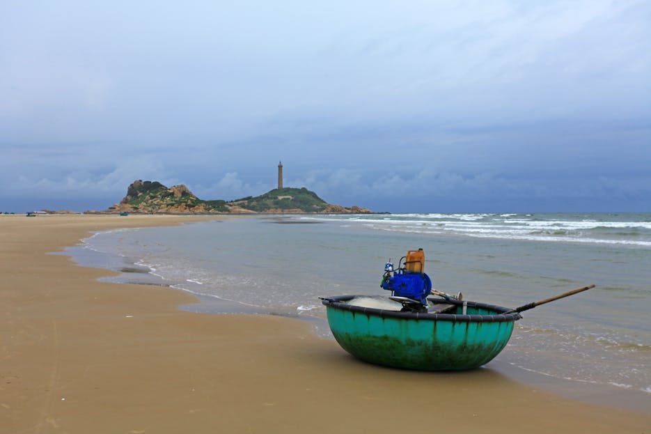 Kulfiy Ke Awaz: Yaadon, A round boat rests on a sandy beach near a lighthouse with a cloudy sky.