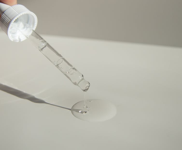 Moonslice Beauty Lip Oil Close-up of a cosmetic pipette releasing serum onto a surface with soft sunlight.