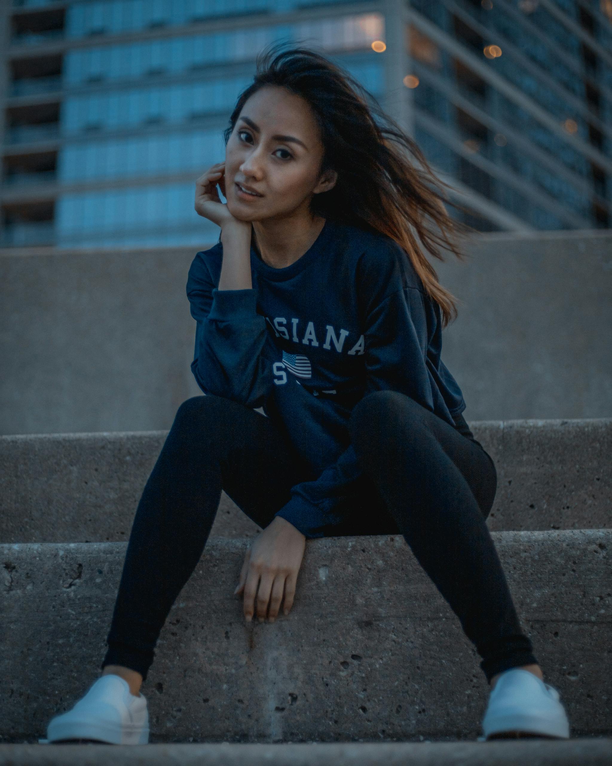 Fashionable woman sitting American Made Jeans on urban steps in Chicago with moody city backdrop.