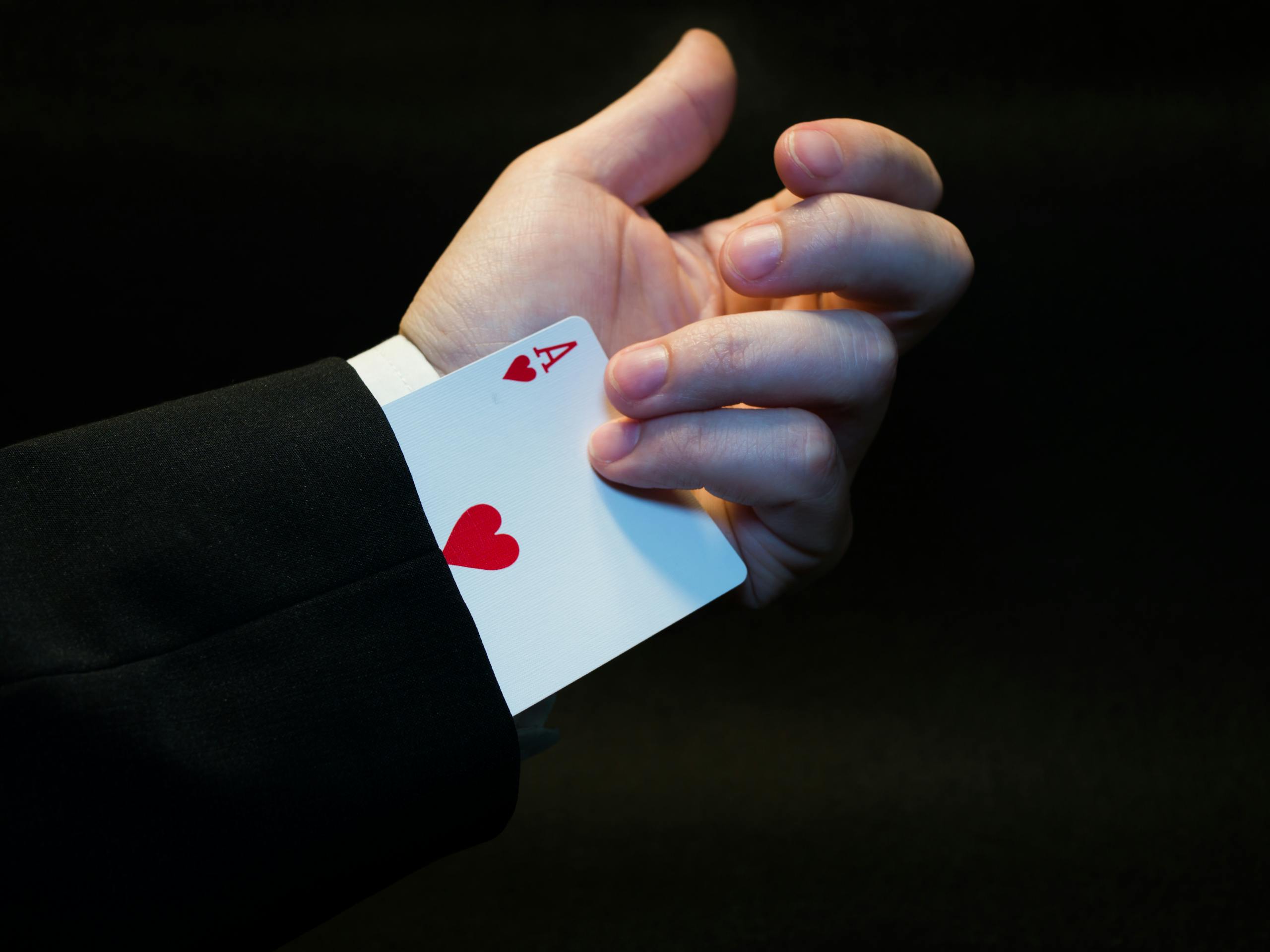 The Techno Tricks A magician's hand showing an ace of hearts hidden up the sleeve, symbolizing magic and trickery.