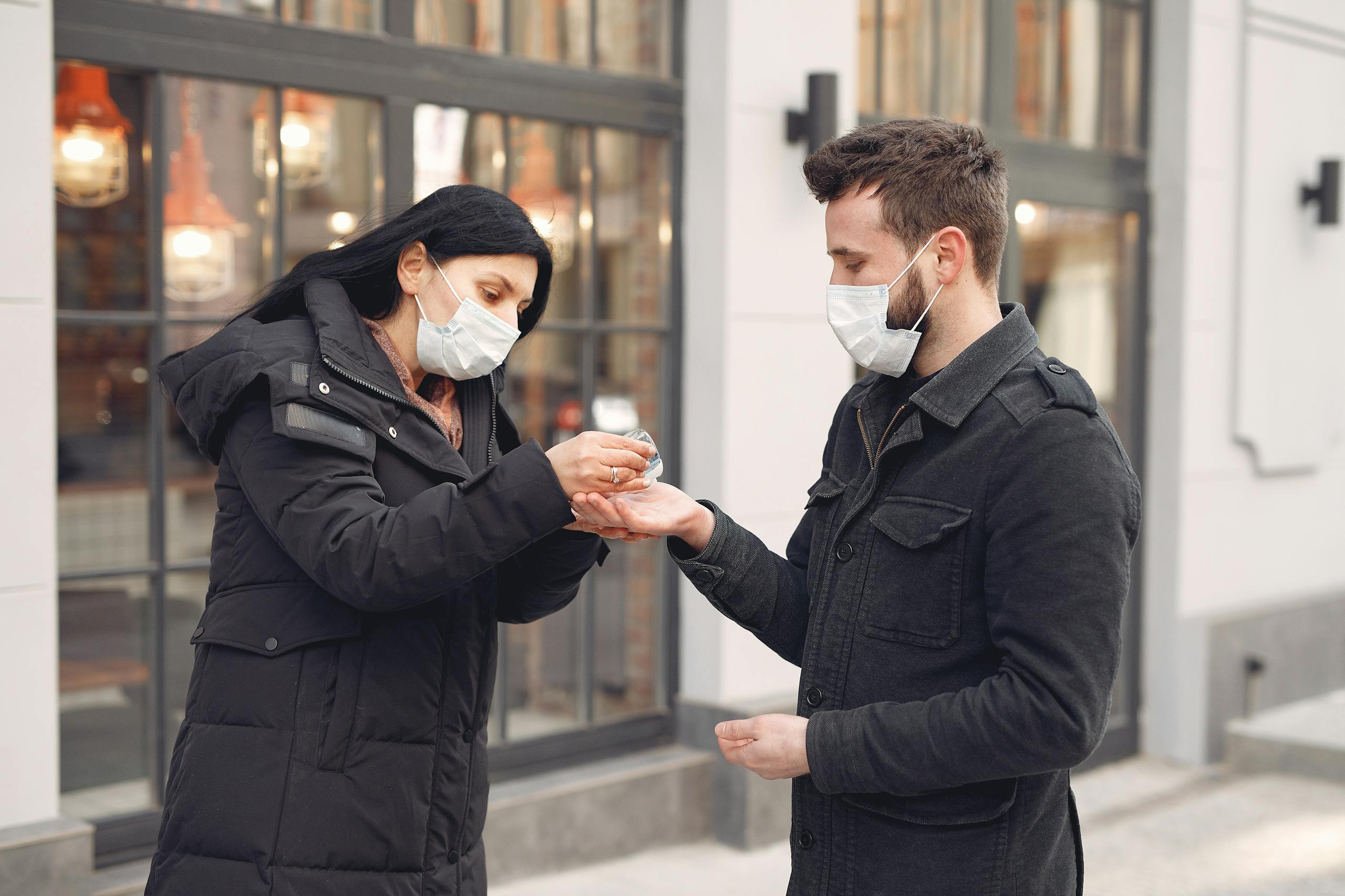 Thealite Keep Safe A man and woman wearing masks using hand sanitizer outdoors for hygiene during COVID-19.