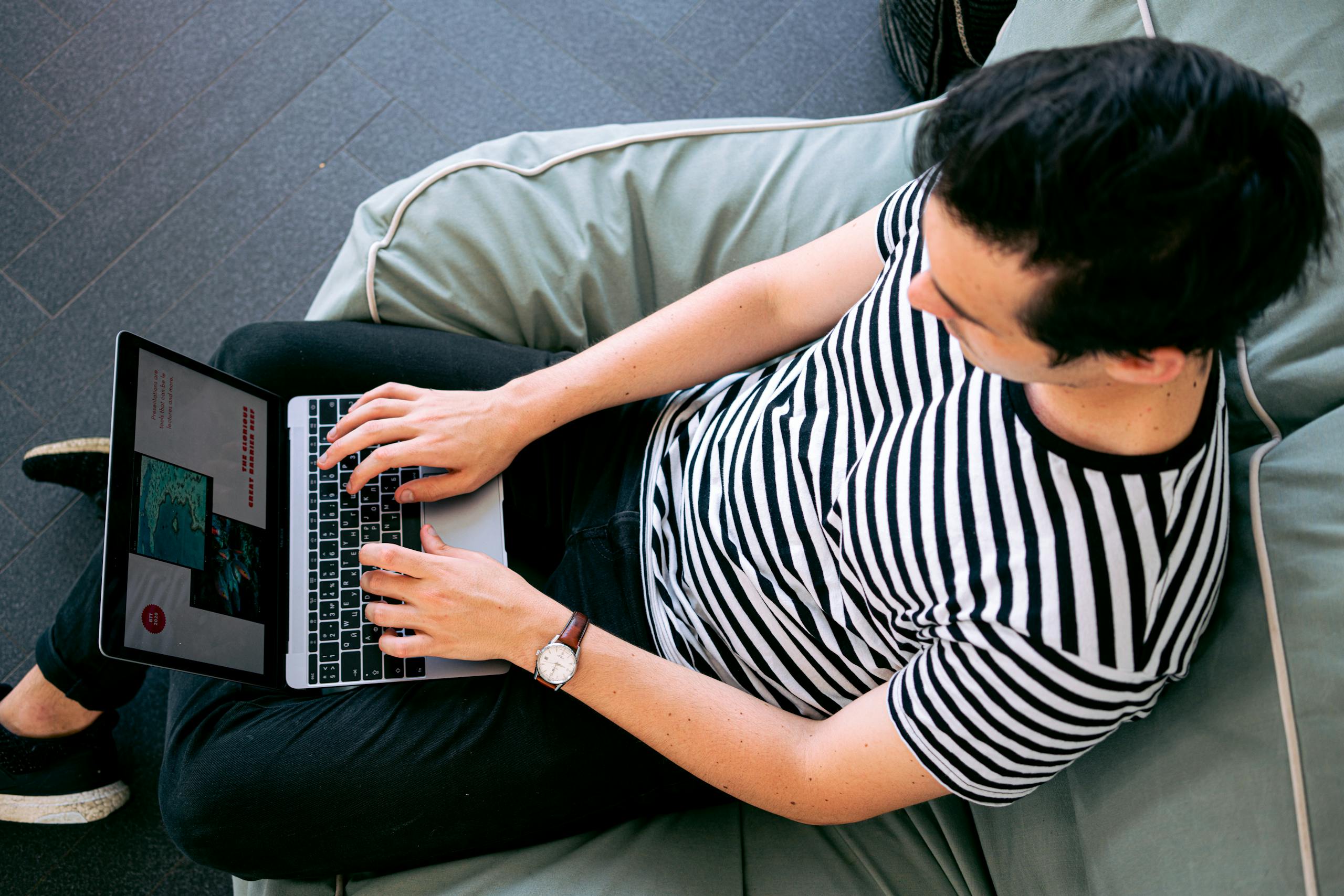 FSI Blogs US A man in a striped shirt using a laptop on a bean bag, embodying relaxed productivity.