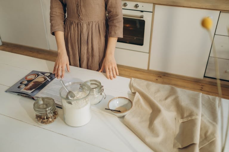 Recipeasy Recipes A person prepares ingredients on a wooden kitchen table with a cookbook for baking.