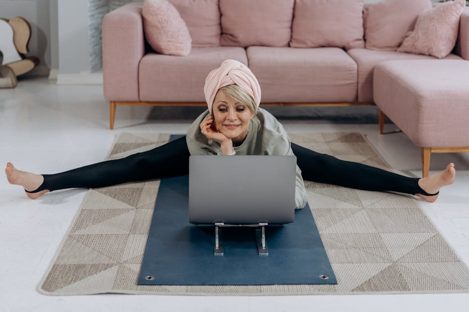 Hrithik Roshan Age A senior woman enjoys a relaxing yoga session indoors, stretching while using her laptop.