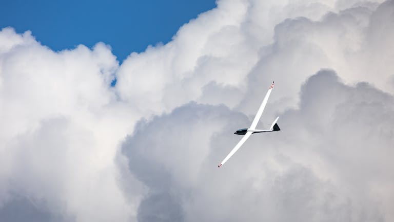 Disclaimer TheAlite A sleek glider flies gracefully amidst the expansive cumulus clouds under a bright blue sky.
