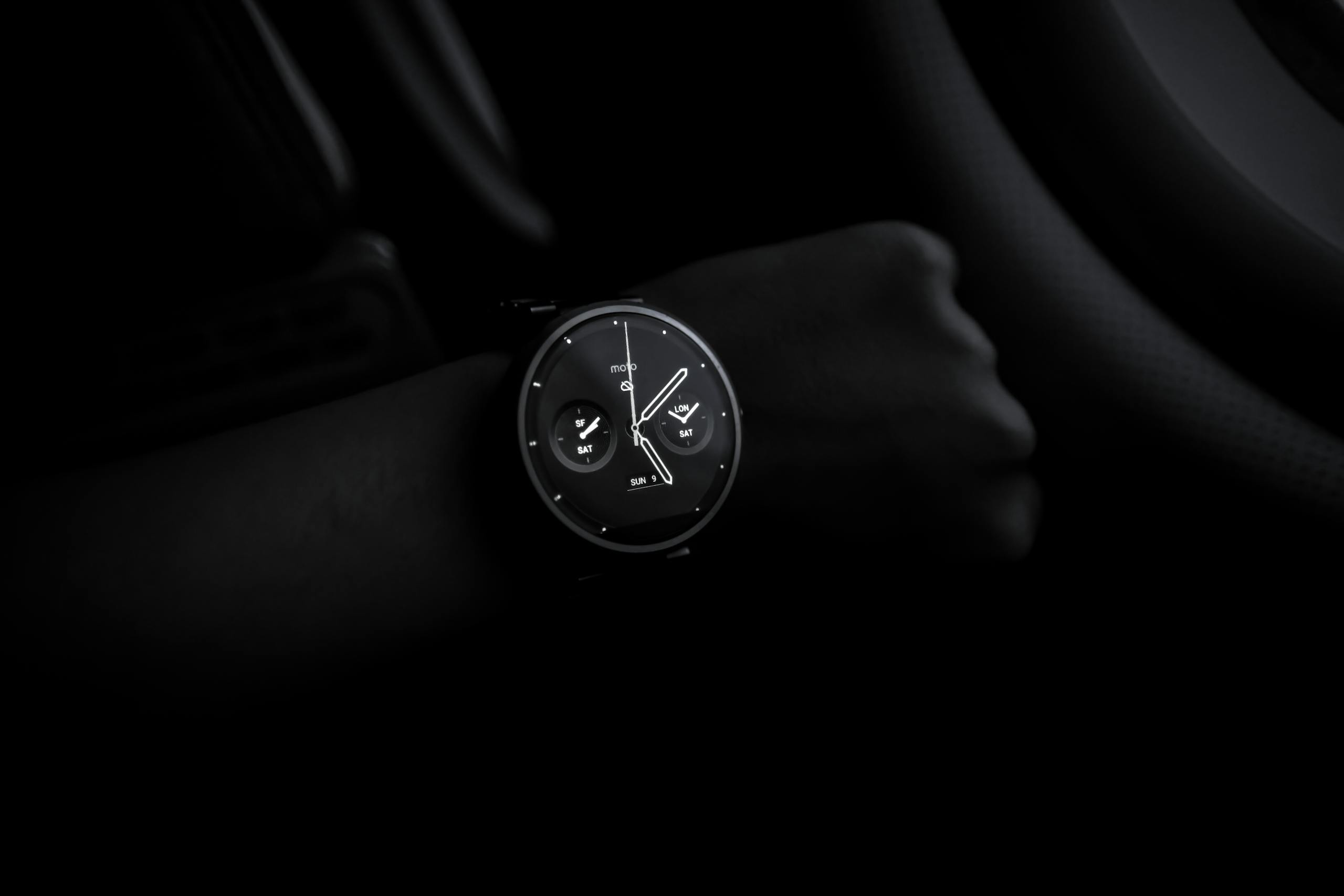 cbybxrf A sleek Moto 360 smartwatch showing time on a wrist in a dimly lit setting, emphasizing its modern design and technology.