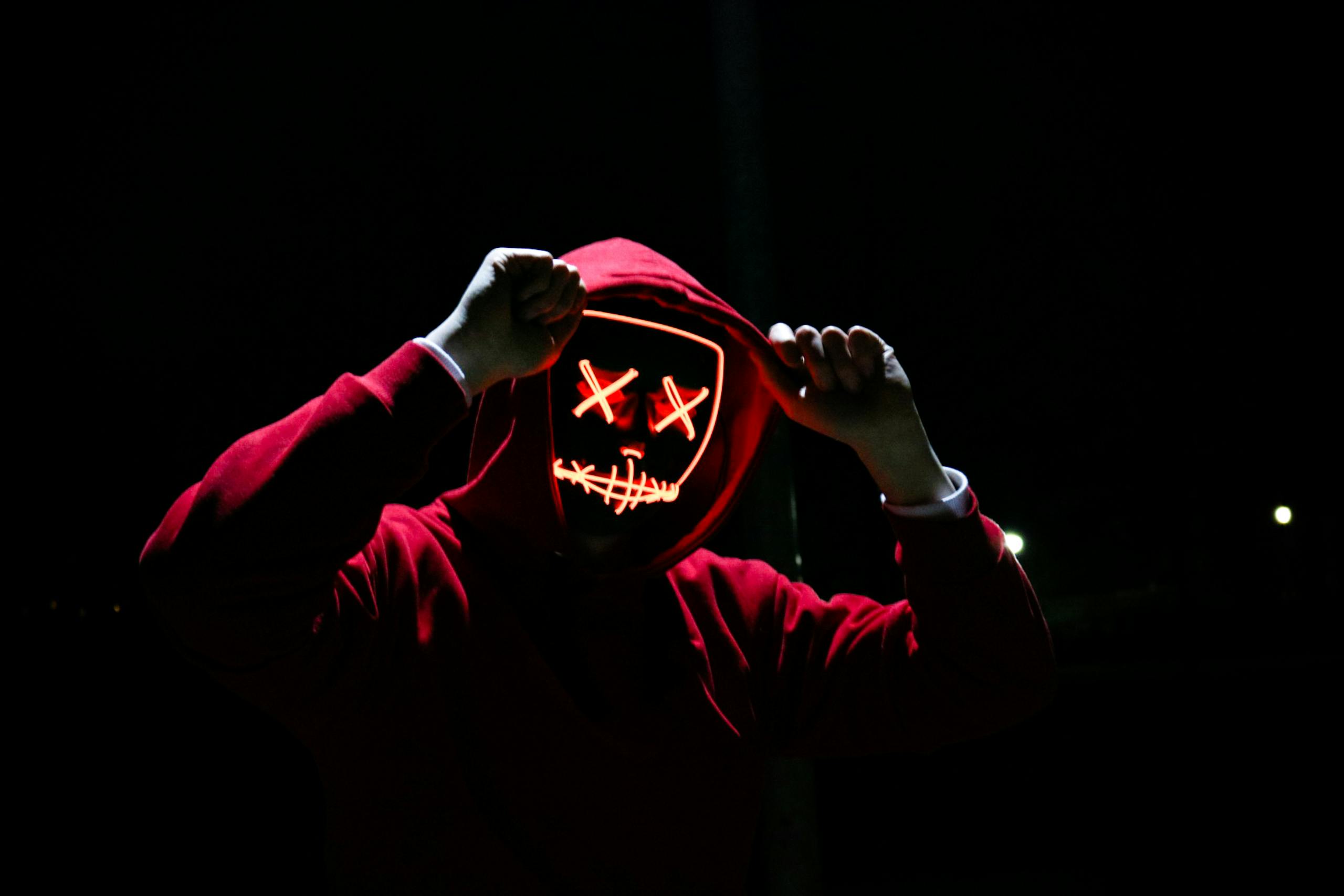 Mozarabic Hoodie A spooky illuminated mask figure with a red hoodie in a dark setting, perfect for Halloween themes.