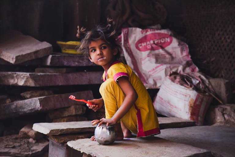 Hanumant Dham: A young girl in yellow clothing brushing her teeth in Chitrakoot Dham, depicting everyday rural life.