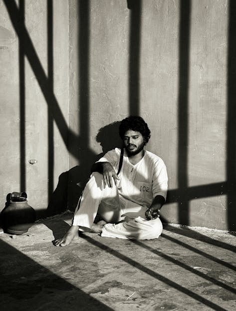 TEK-102 Black and white photo of a man in prison uniform sitting pensively, shadows cast on the floor.