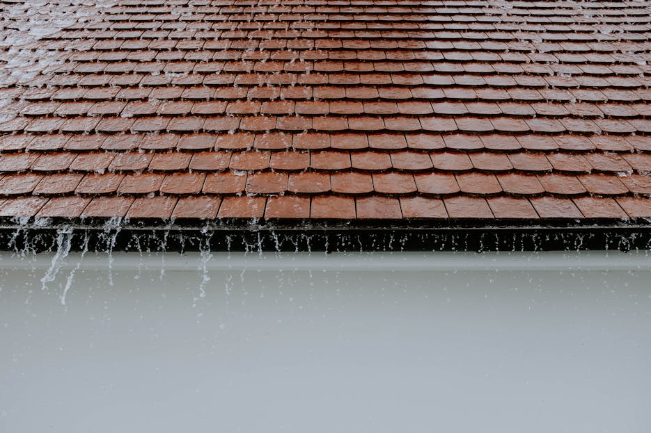 Trencher for Drainage Brown roof tiles with rainwater cascading down, showcasing architectural texture and detail.