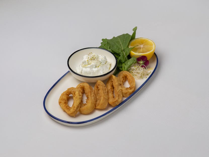 Calamariere Delicious crispy calamari paired with creamy tzatziki, lemon, and greens on a plate.