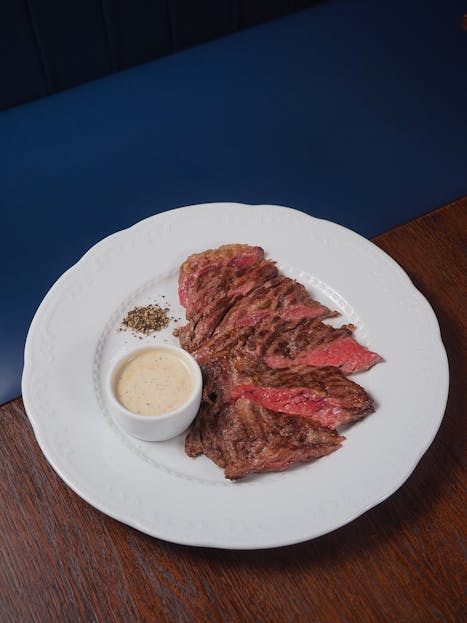 Gastroshiza Deliciously grilled steak served with creamy sauce on a white plate.