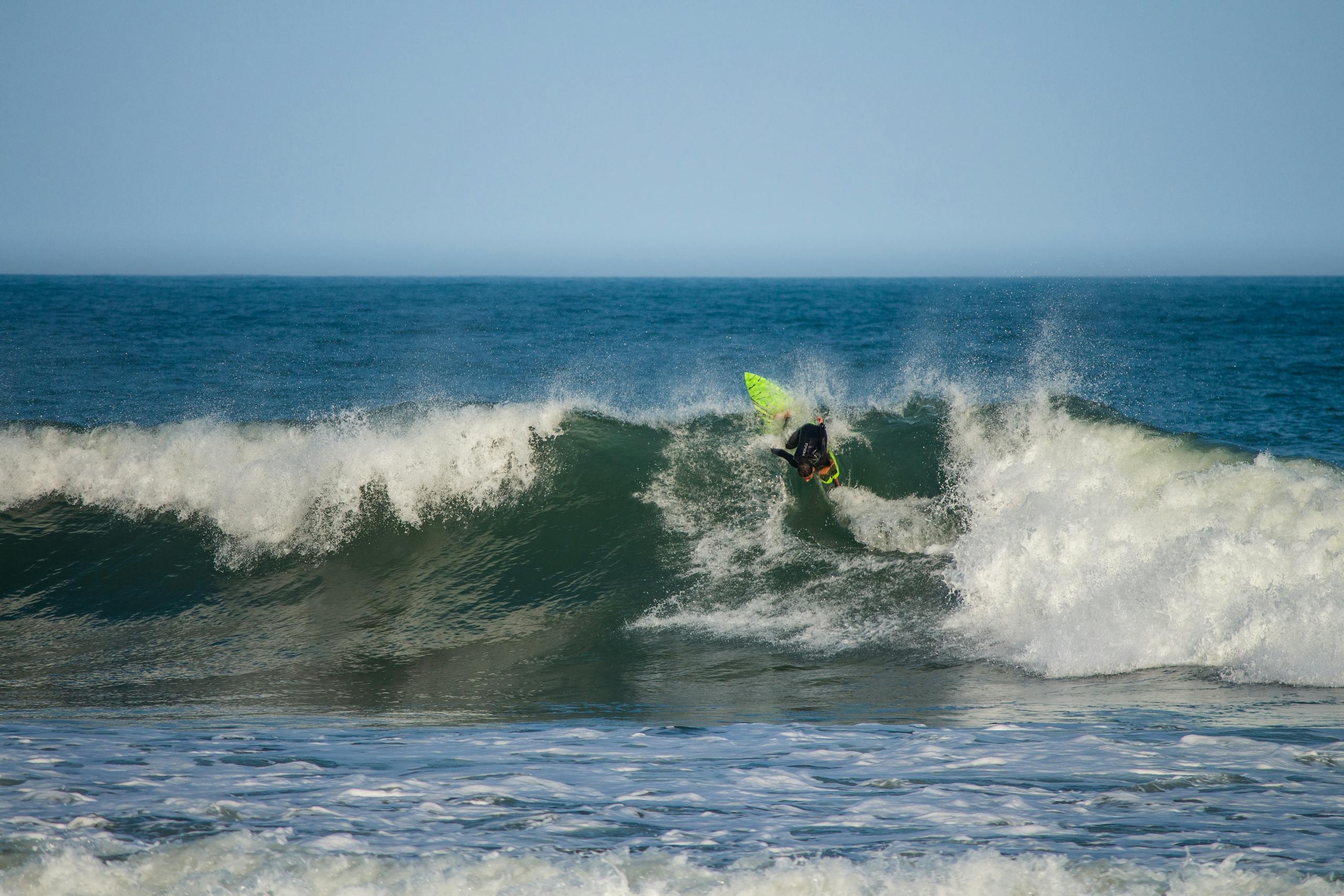 Vitilinox Faceless surfer wearing black wetsuit on surfboard balancing on surfboard on splashing waves of endless azure sea on clear summer day