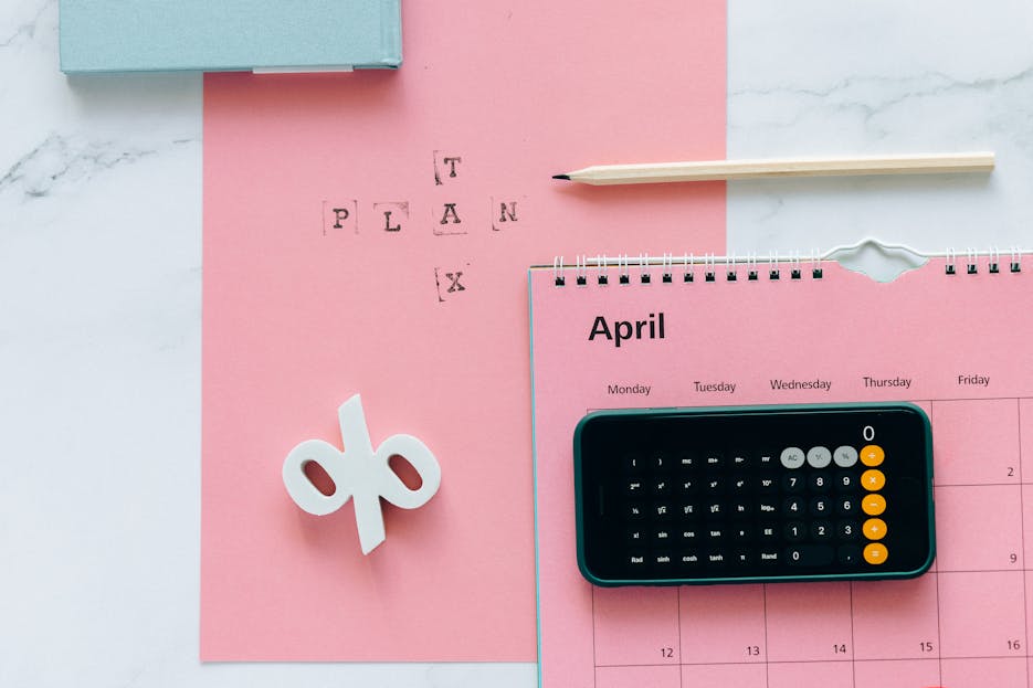 88Magazine Flat lay of April calendar with calculator, pencil, and pink background for financial planning.