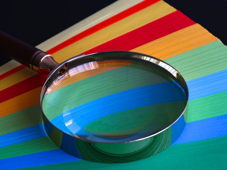 DiscoverHeading Magnifying glass resting on vibrant rainbow-colored paper close-up.
