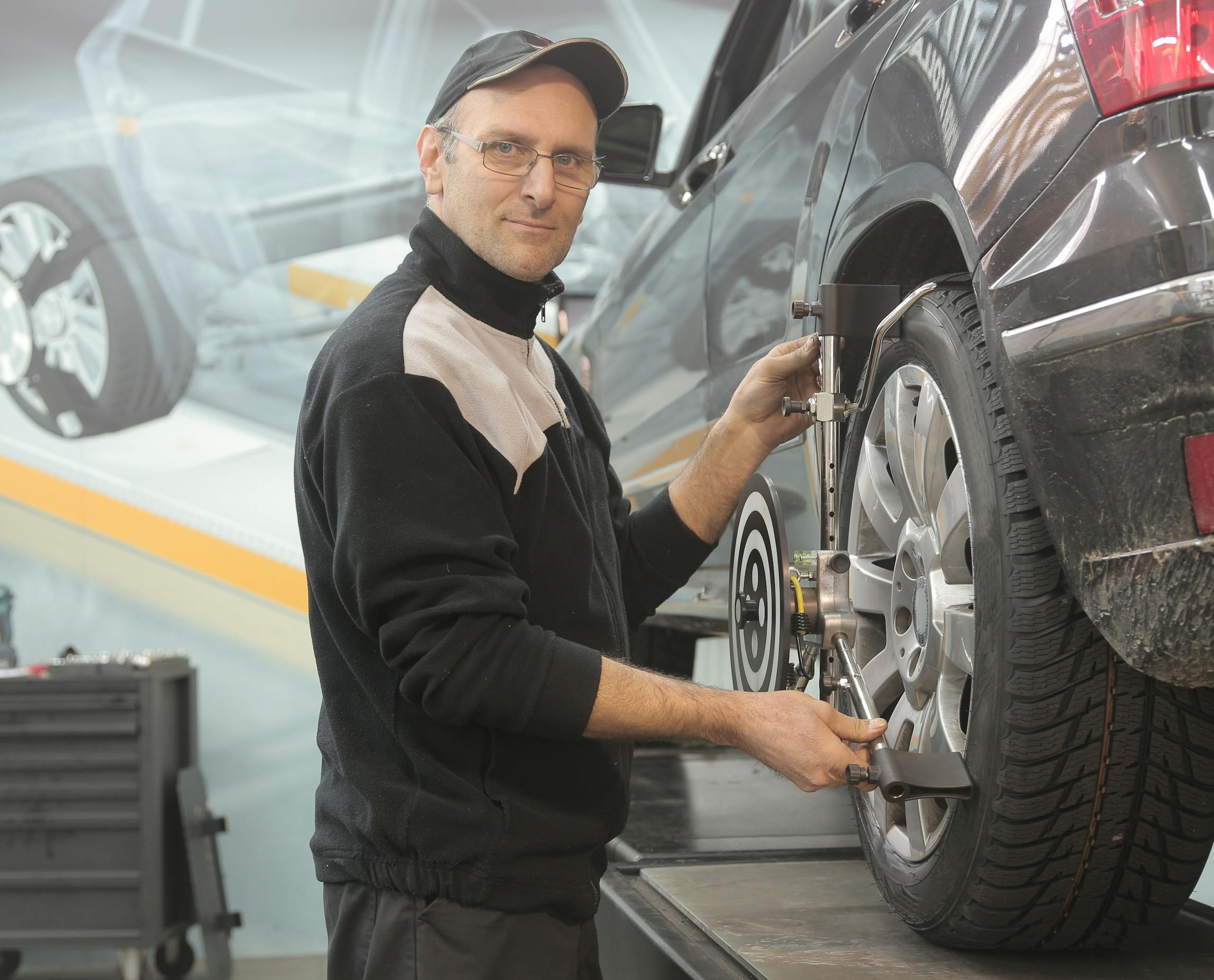 Magento Service Gonzay Mechanic performing wheel alignment on a car in a professional garage setting.