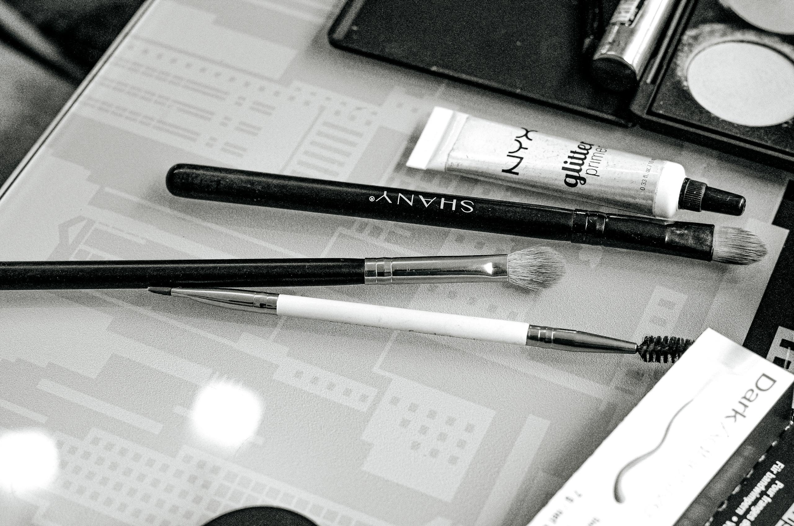 Shani Levni Monochrome image showing makeup brushes and cosmetics on a glass table.