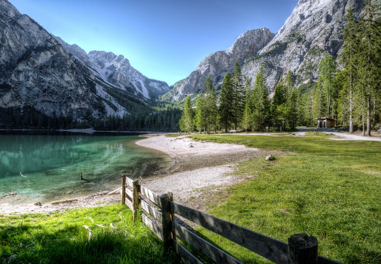 Cartetach Serene mountain lake with green trees and a rustic fence, perfect nature backdrop.
