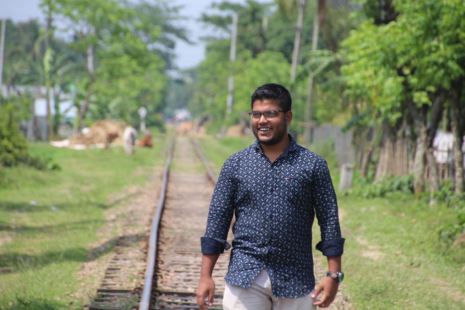 SEO by Highsoftware99.com 2026 Smiling man casually walking on railway tracks surrounded by lush greenery in Jamalpur, Bangladesh.