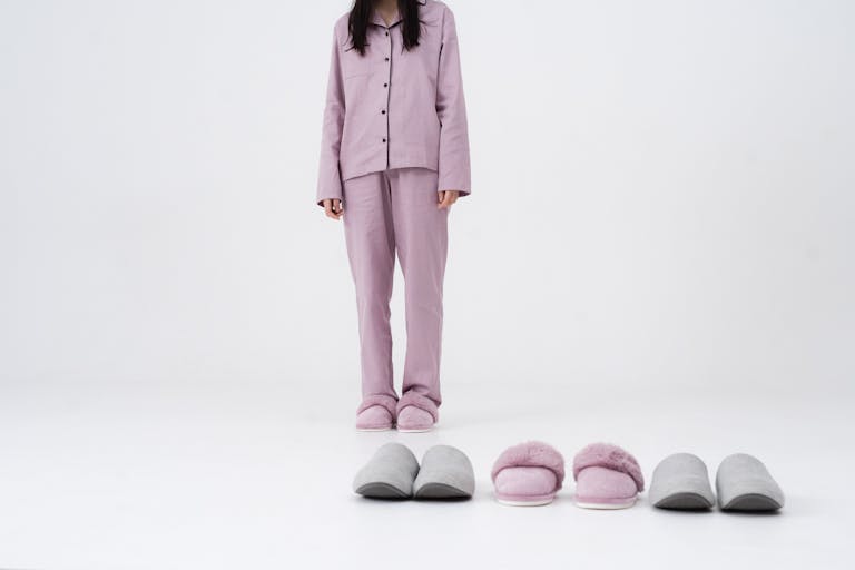 Kappa Delta Slippers Stylish woman in pink pajamas standing with multiple slippers in a studio setting.