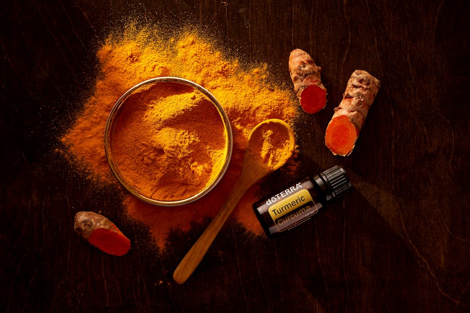 Well Health Organic Ayurveda Top view of turmeric powder, curcuma roots, and essential oil on wooden surface.