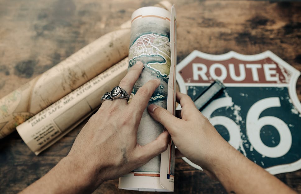 Veganov Trichy Two hands holding vintage maps of Route 66 on a wooden table. Perfect for travel and history themes.