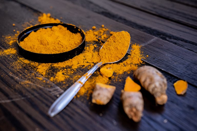 Well Health Organic Ayurveda Vibrant turmeric powder and root on a dark wooden surface, emphasizing natural spices.