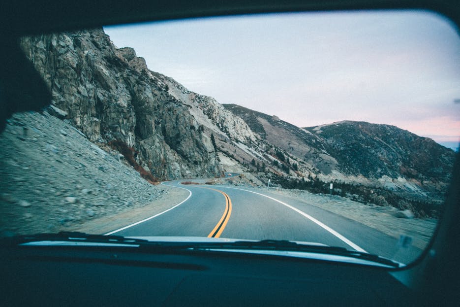 Meilaier View of a winding mountain road through a car windshield during a road trip.