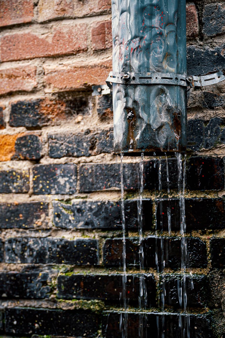 Txmyzone Water flows from a weathered pipe on a rustic brick wall, capturing urban charm.