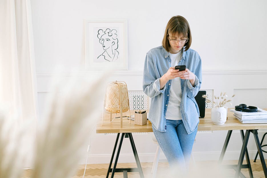 FSI Blogs US Woman in denim using smartphone in a bright home office setting.