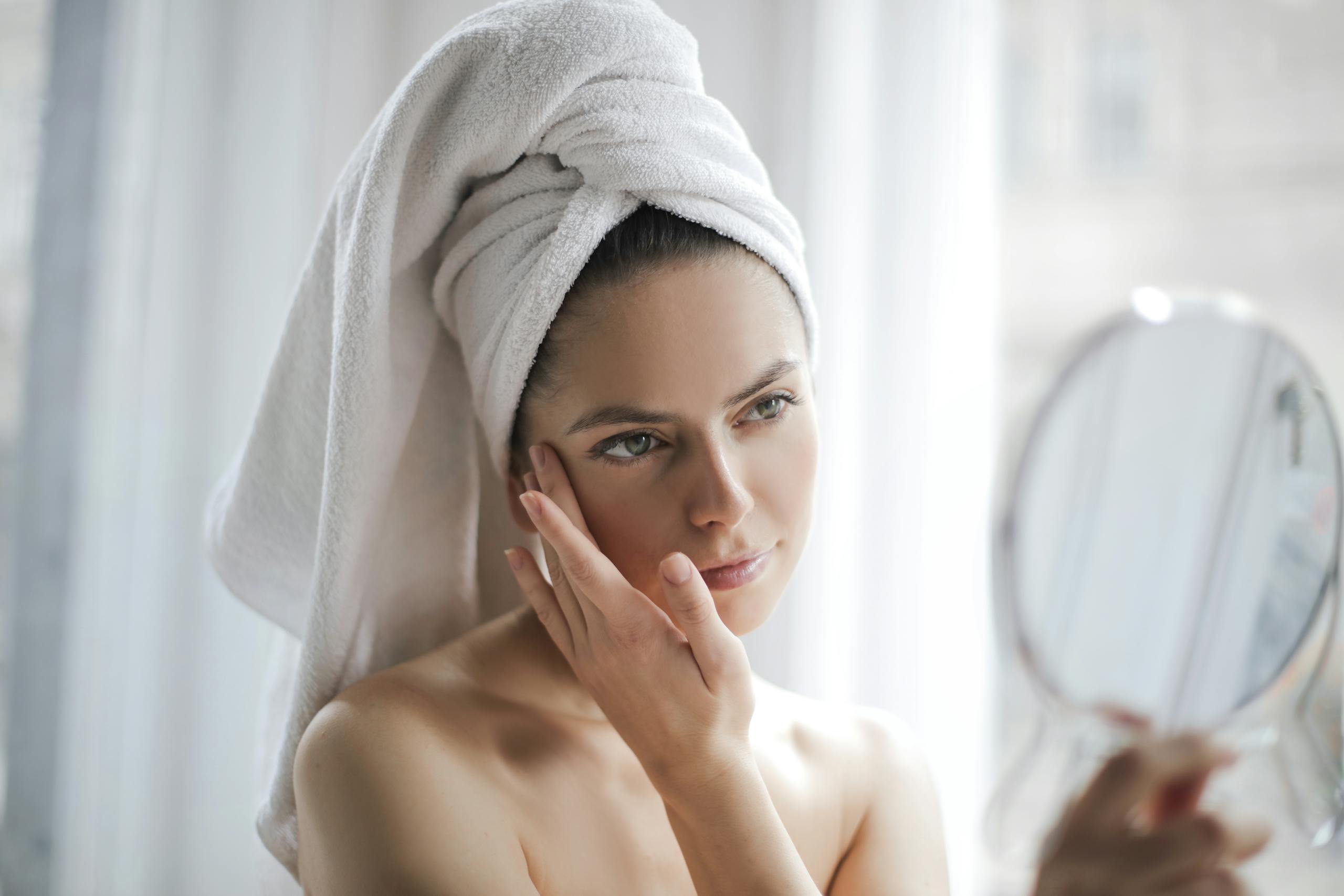 Beauty Tips – Well Health Organic.com Young female with bare shoulders and towel on head holding small mirror and checking skin with it in bathroom