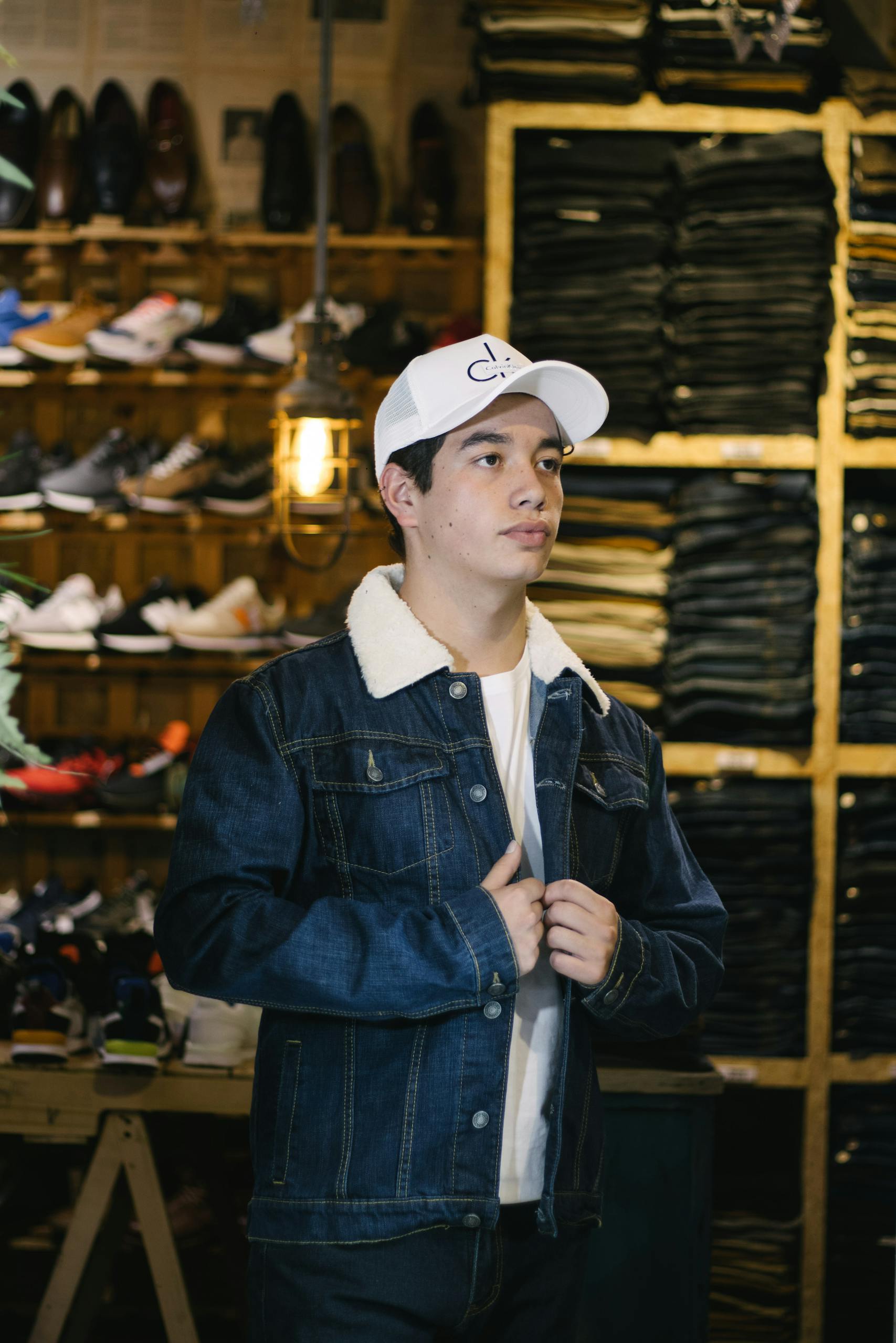 Babyfied Apparel Young man in denim jacket and white cap shopping in a stylish clothing store.