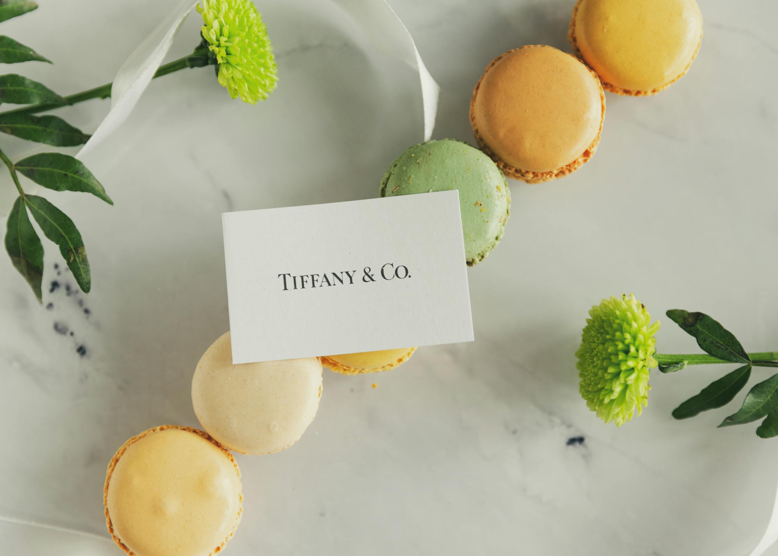ibomma1.co Close-up of colorful macarons and greenery with Tiffany & Co. card, on marble.