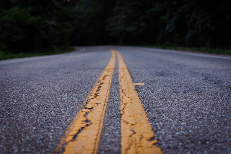realize infrastructure navigator Scenic close-up shot of an empty asphalt road with yellow lines curving through a forested area.