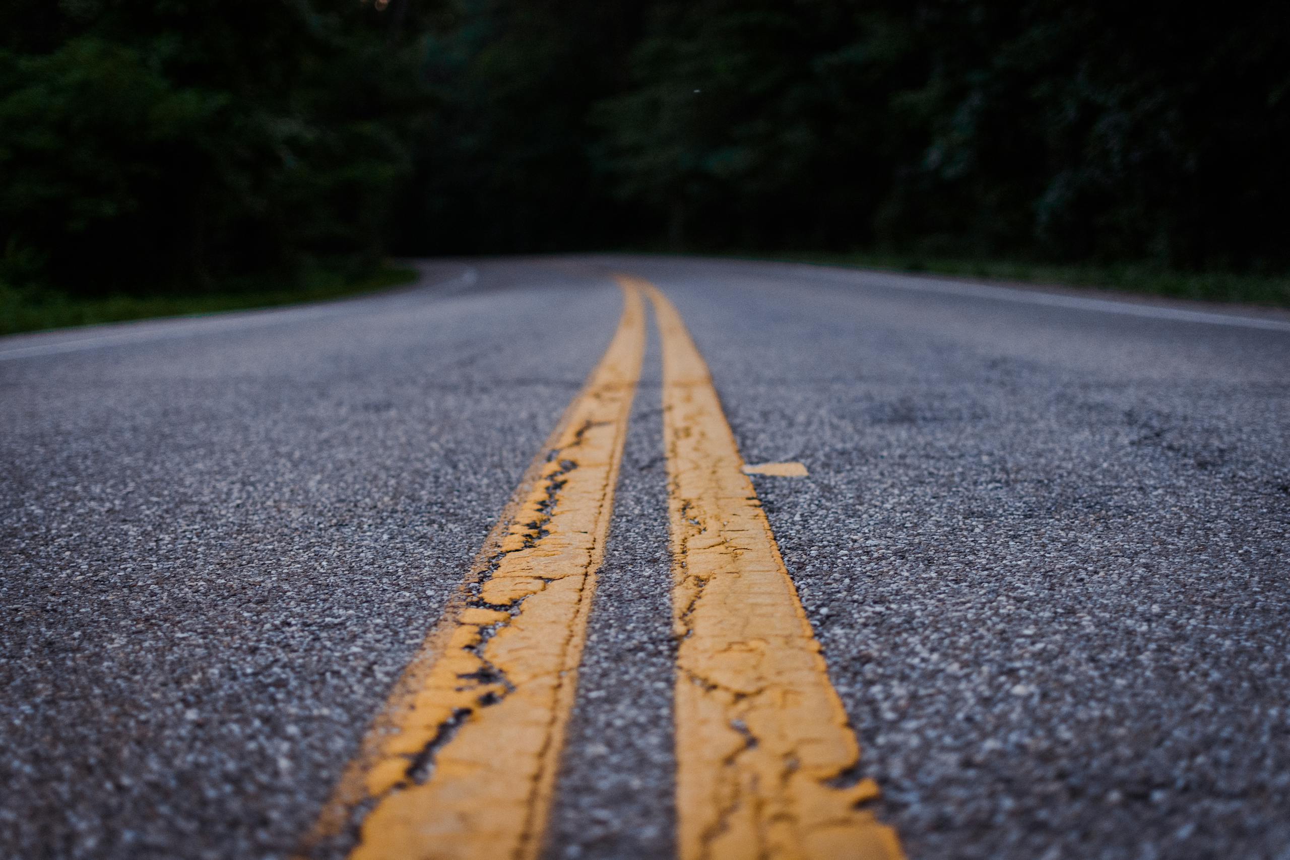 realize infrastructure navigator Scenic close-up shot of an empty asphalt road with yellow lines curving through a forested area.