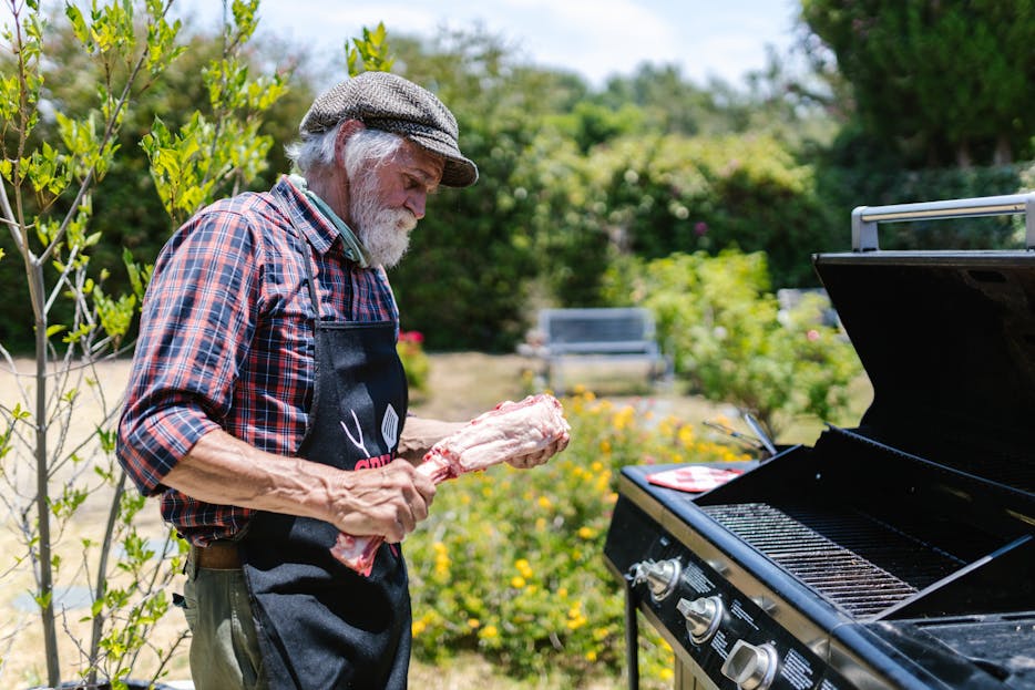 weber grillvorführung Senior man cooking meat on a gas grill in a sunny garden, enjoying a relaxed outdoor day.
