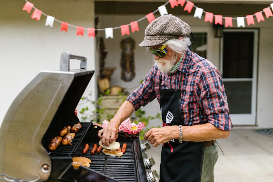 weber grillvorführung Senior man preparing burgers and hot dogs on a barbecue grill outdoors.