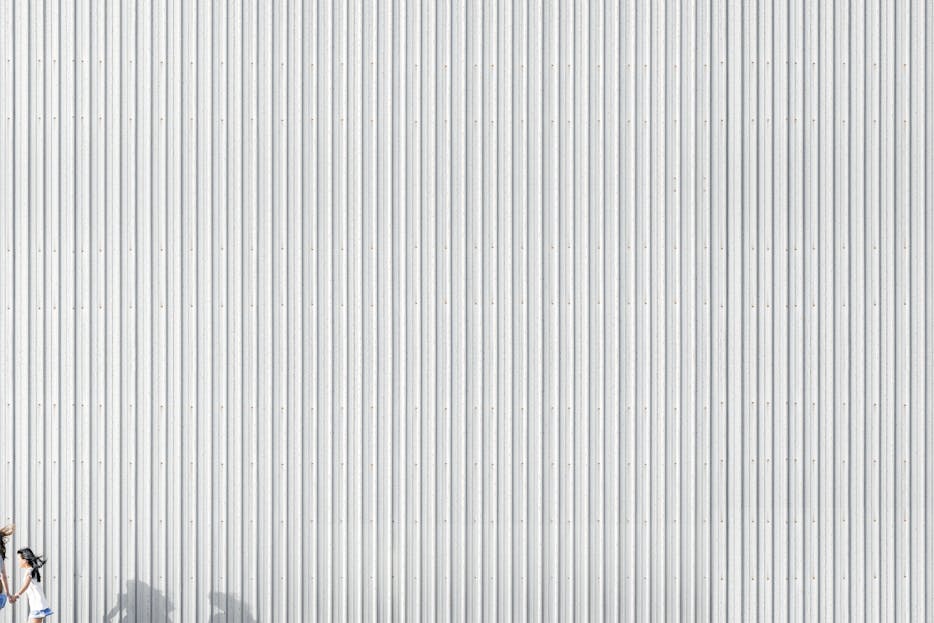 Emfyteymata Silhouette of a woman running against a corrugated metallic wall, showcasing minimalist design and light play.