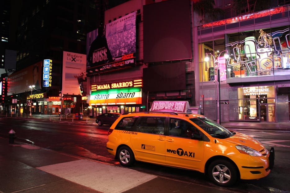 Kulfiy com Yellow NYC taxi cab parked in vibrant Times Square, New York City streets at night.