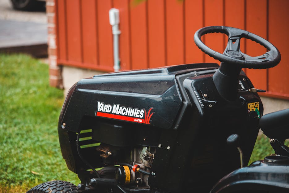 Grassland Mower Detailed view of a Yard Machines riding lawn mower parked on grassy lawn beside a red shed.