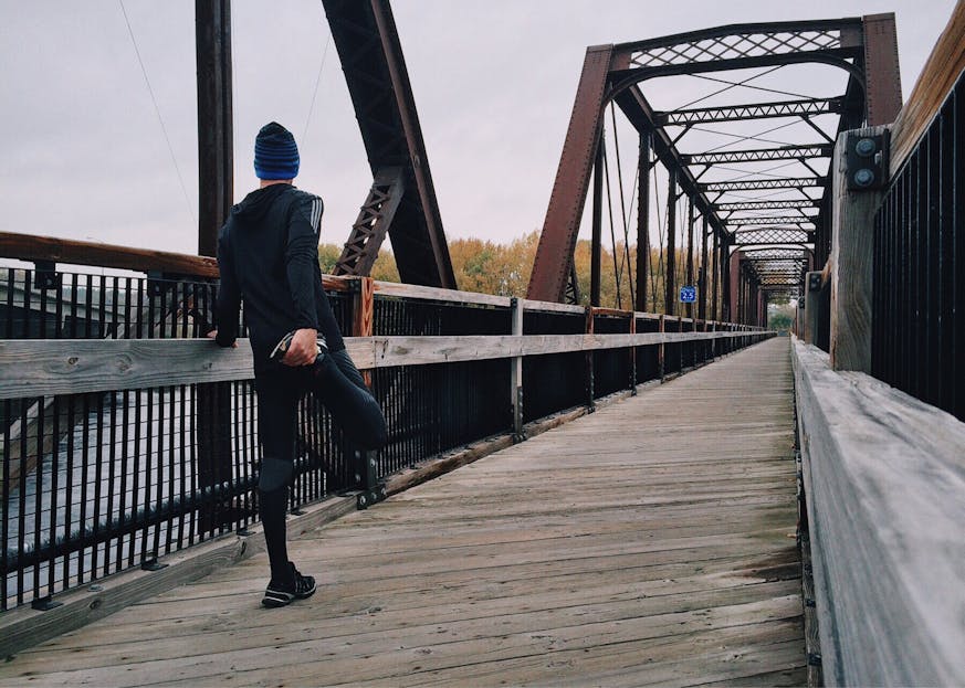 Voozon Man stretching on a wooden footbridge during a daytime run on an iron bridge, emphasizing fitness and recreation.