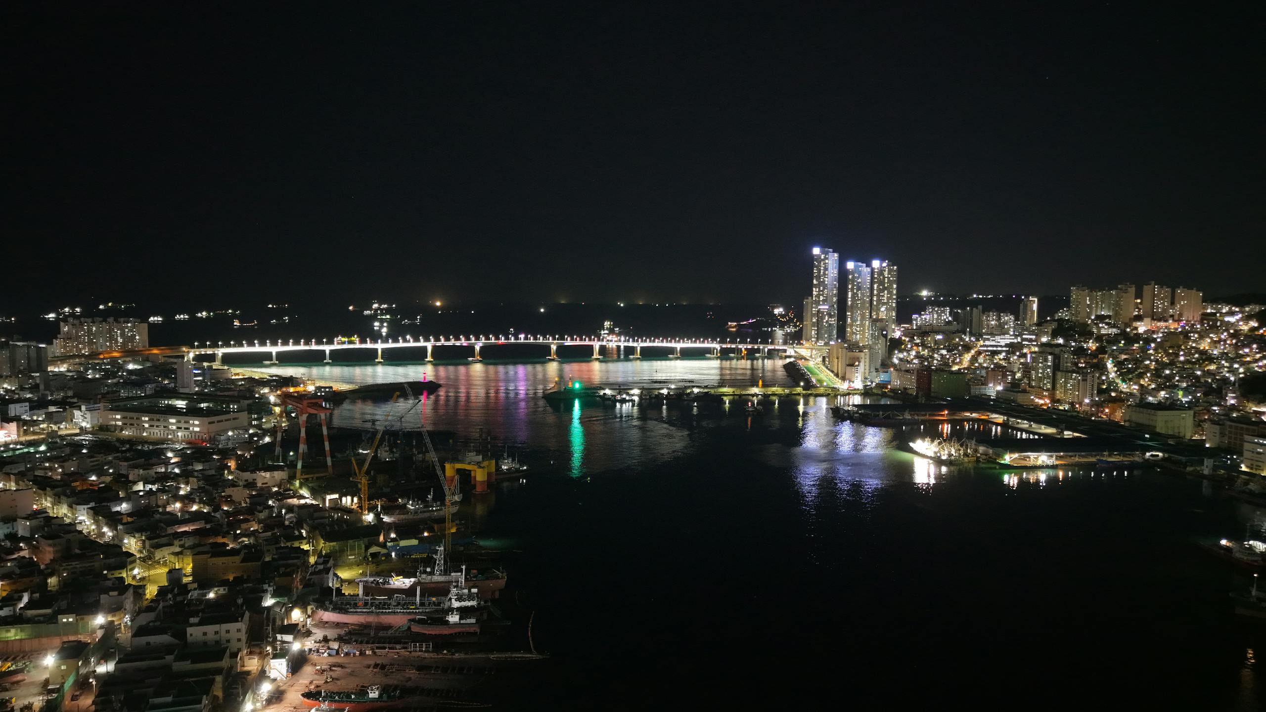 The Vzusa Stunning night view of Busan's illuminated skyline and bridge reflecting on the water.