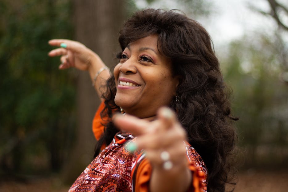 Lupe Gidley A joyful African American woman smiling and gesturing outdoors in Decatur, Alabama.