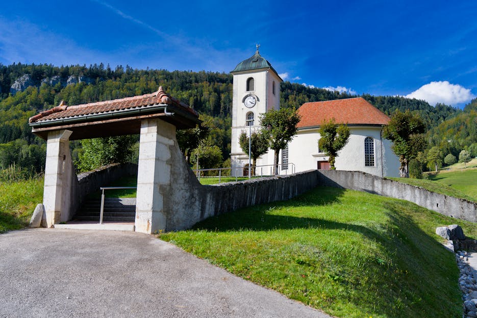 Enntal A picturesque Swiss church nestled in a lush valley against a mountain backdrop on a clear summer day.