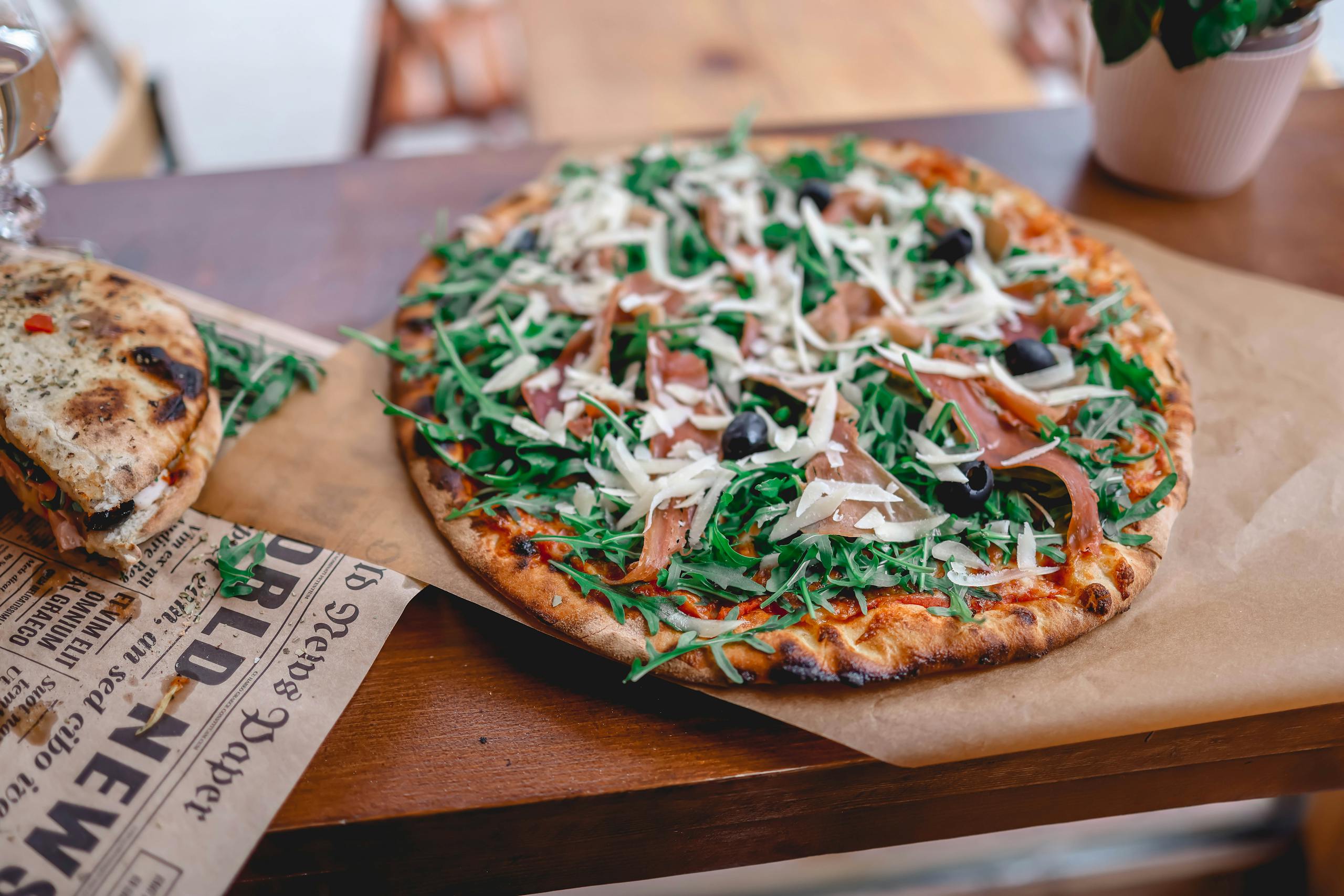 Pizzerija Plus A tasty prosciutto and arugula pizza served on a wooden table, perfect for food photography enthusiasts.