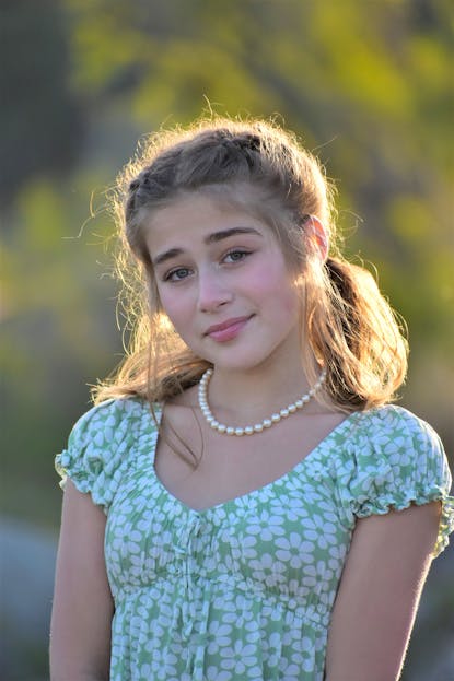 Finley Elaine Griffin A teenage girl with long brown hair poses outdoors, wearing a floral dress and pearls.
