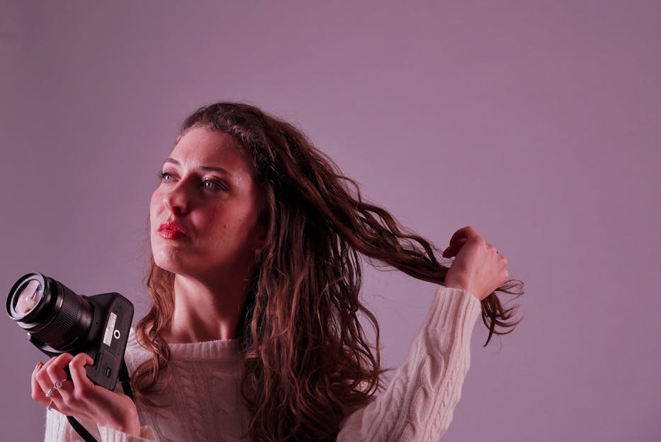 Gianetta Fluent A woman in a white sweater holding a camera, captured in warm studio lighting.